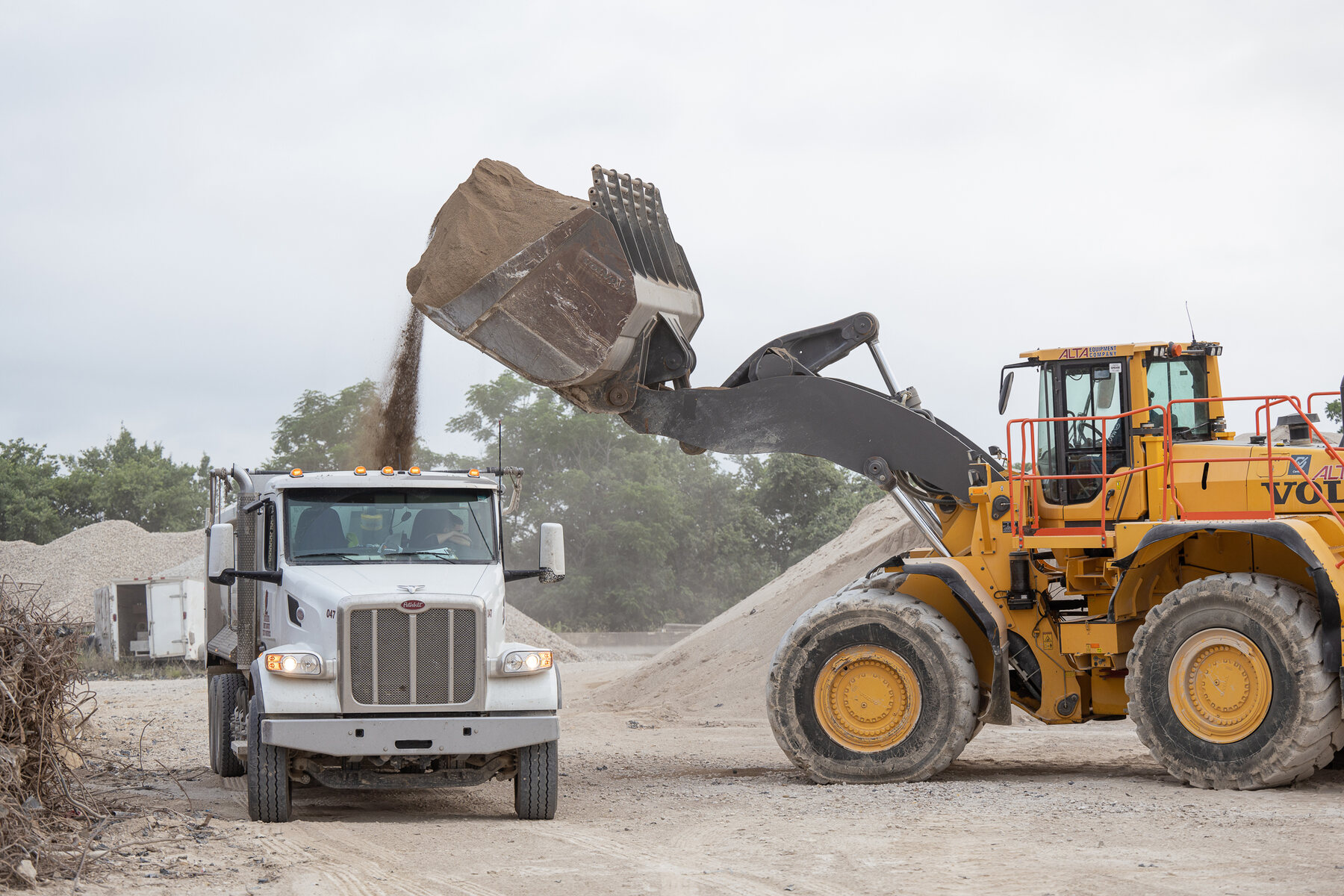 A wheel loader dropping aggregate into a dump truck at the stockpile